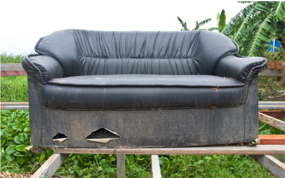 An old and worn-out sofa placed on some wood planks in a field