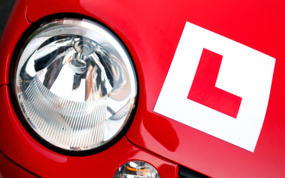 A close up of the front headlight of a red car with a learner driver sign attached