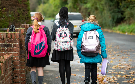 Three girls walking along a pavement wearing school uniform and backpacks