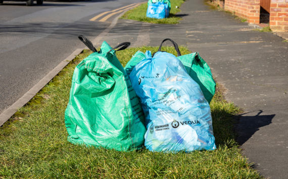 Green recycling bag and blue waste bag on curb