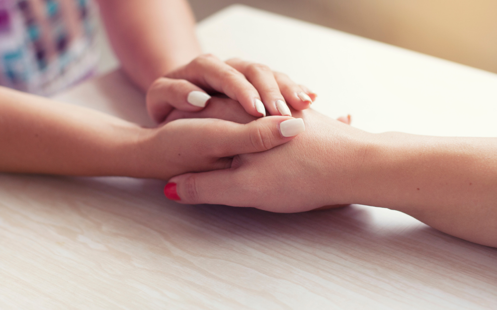 A hand laid on a table, being held by another hand to show support