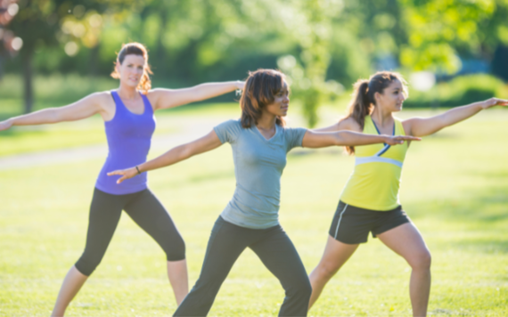 Three women practicing yoga poses outside in a park