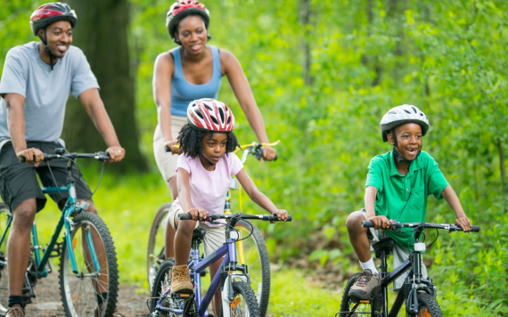 Two adults and two children cycling through a tree lined area