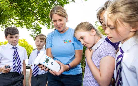 Five pupils in school uniform look at a hand-held monitor held by active travel officer