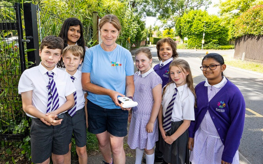 A group of pupils and an air quality officer smile for the camera while holding portable air pollution monitoring equipment.