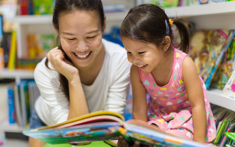 A mother helps her young daughter read a book