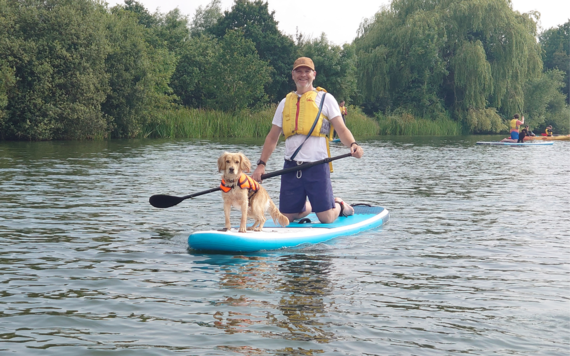 A photo of a man and a dog on a paddleboard on the lake of Dinton Pastures