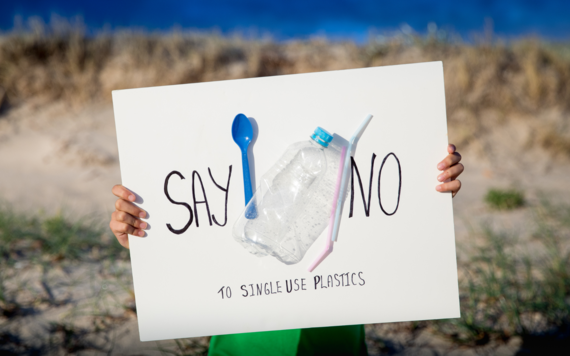 Hands holding a signboard with the words say no and ten single-use plastics. There are a plastic straw, fork and bottle on the board