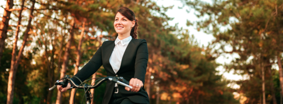 photograph of a female cyclist in business attire cycling through a wooded area on a sunny afternoon