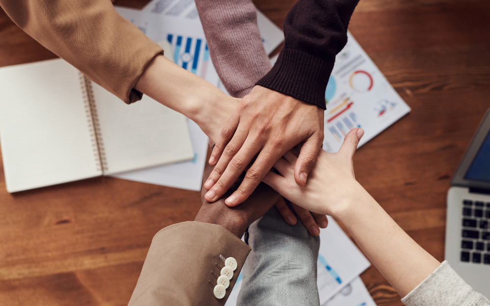 Five hands put together in a stack over a desk