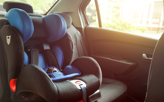 An empty carseat in the back of a car with sun shining through the window