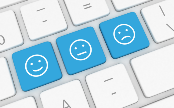 Close up of computer keyboard with three blue buttons showing a smiley, neutral and sad face