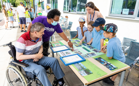 A worker from Optalis with a man in a wheelchair talking to four pupils and a teacher, looking at the pictures of their school