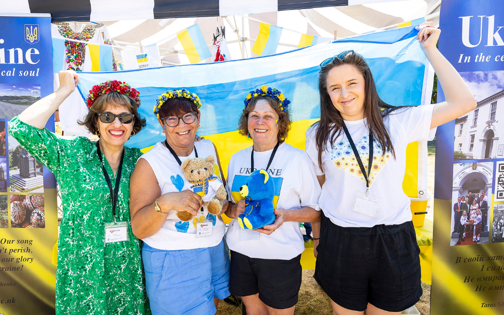 Four women holding a Ukraine flag and teddy bears in the colours of the Ukraine flag smile at the camera