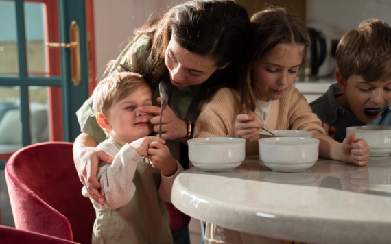 A mother helping her two sons and daughters eat their breakfast