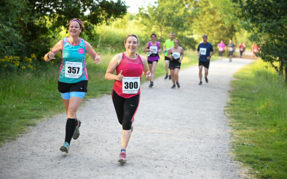 Two female runners of previous Barnes Fitness Dinton Summer Series in the foreground, and several runners in the background