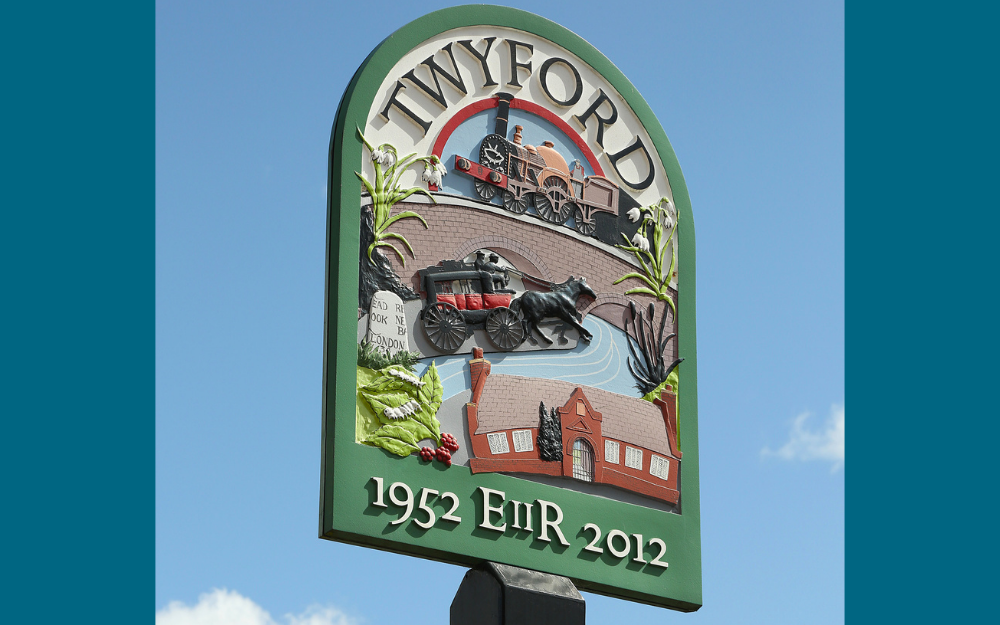 A sign for the parish of Twyford, showing a building, the river, a train and a horse and carriage