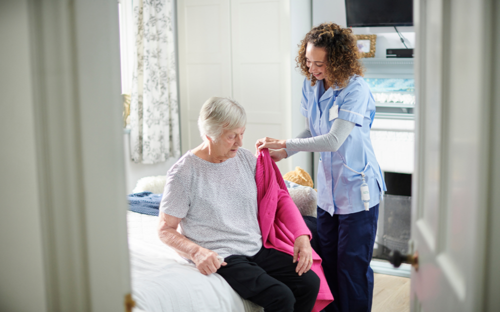 A carer helps an older lady to put on a cardigan 