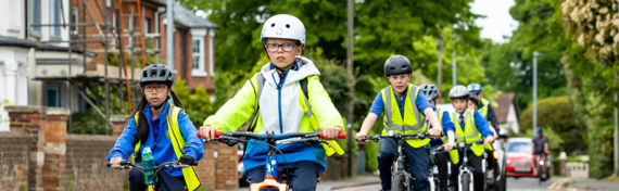 wide photo of children riding bicycles while wearing high-vis gear and helmets