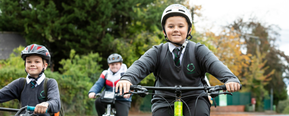 three children riding bicycles and smiling while wearing school uniform and bike helmets