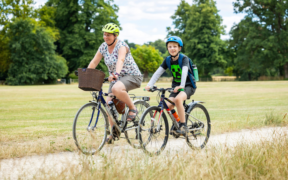 two people cycling along a path alongside a park