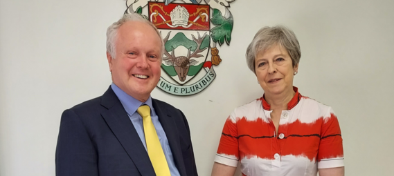 Council leader Clive Jones and MP Theresa May stand together smiling in front of the WBC crest