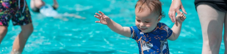 a small child reaching for a ball (out of shot) in the paddling pool at California Country Park