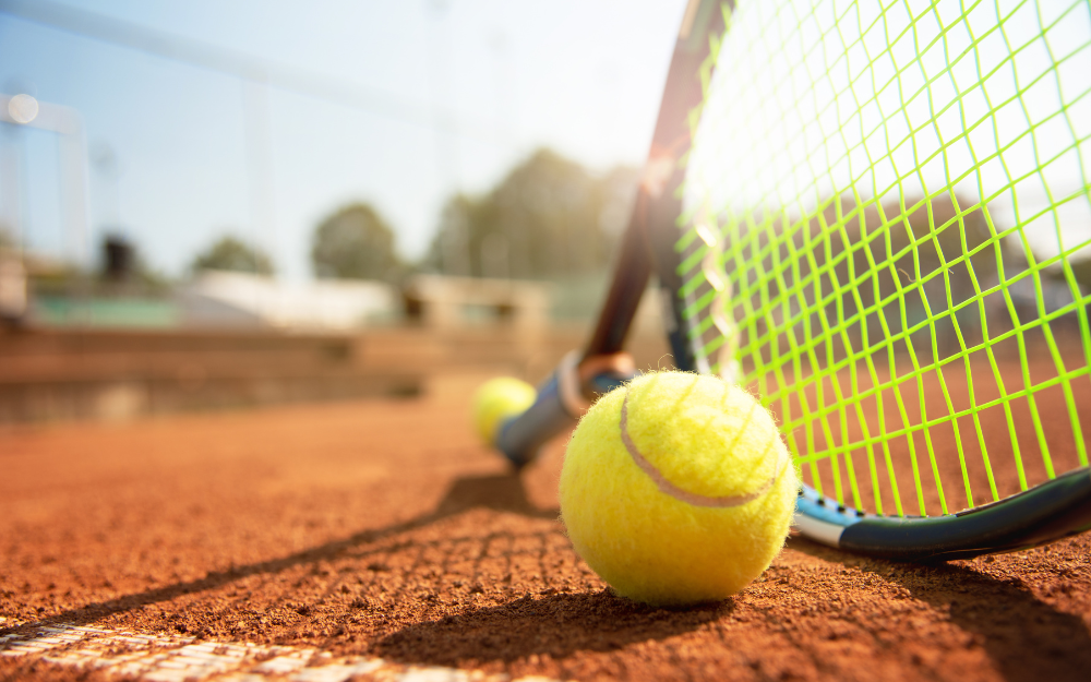 A tennis racket and ball on a clay court, next to the net