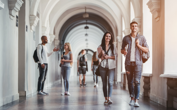 Four university students are walking in a hallway and two are talking to each other