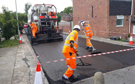 Three workers in high viz clothing smooth out a newly micro resurfaced road