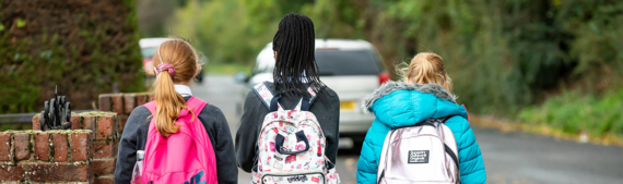 shot from behind of three school-aged girls walking down a street wearing backpacks