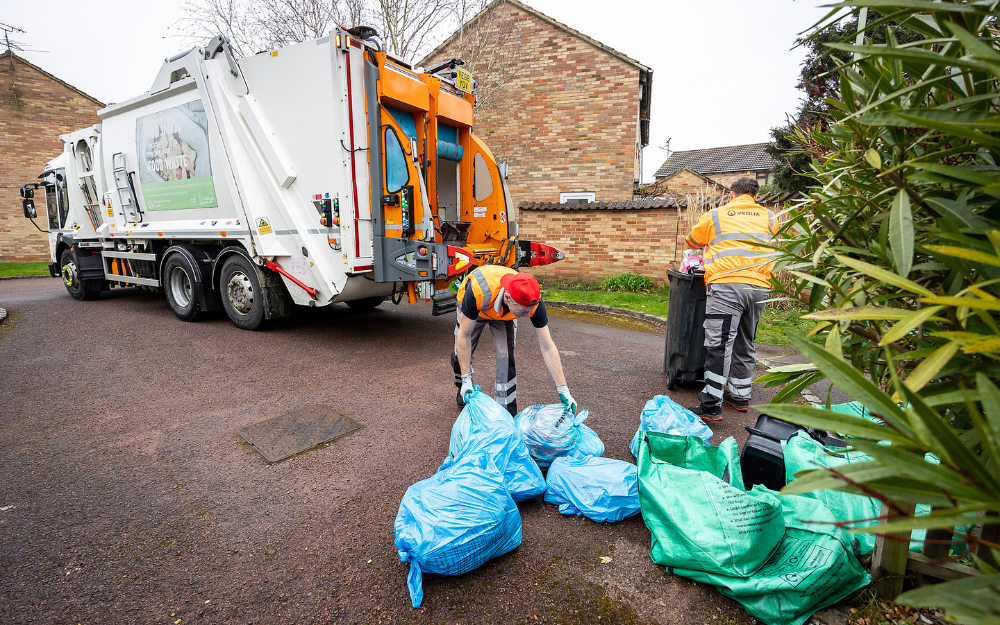 Waste collection crew rounds up blue bags, food waste and recycling to put into a waste truck