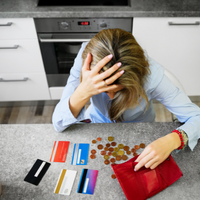 Woman clasping her head in despair as she looks at credit cards and counts money in purse
