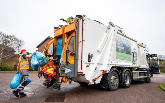 A crew member putting blue rubbish bags into the back of a waste truck