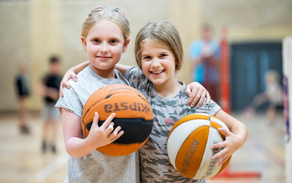 Two girls smith to the camera holding basketballs