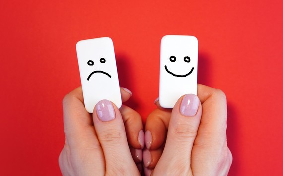 A person holds a white tile in each hand. The tile on the left has a sad face on it. The tile on the right has a happy face on it.