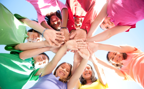 Eight children in different coloured tshirts holding their hands in the middle taken from below