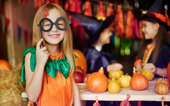 A girl in Halloween costume smiling in the foreground and another two dressed like a witch in the background