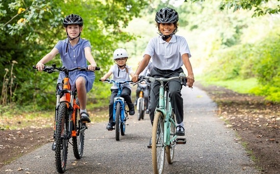 three children wearing helmets smile for the camera while riding along the new greenway at Woosehill