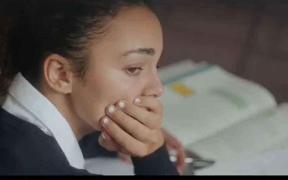 A young girl rests her head on her hand while reading a textbook at school