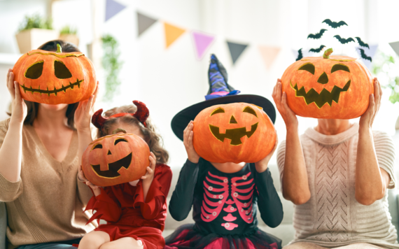 Two kids dressed in Halloween costume in the centre, with two women on their two sides. All are holding up a pumpkin