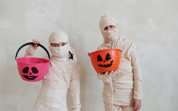 Two people dressed in mummy costume each carrying a Halloween treat bucket