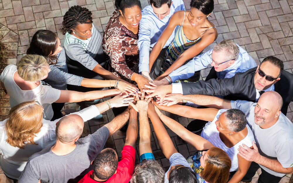 A diverse group of people palce their arms in the centre of a circle