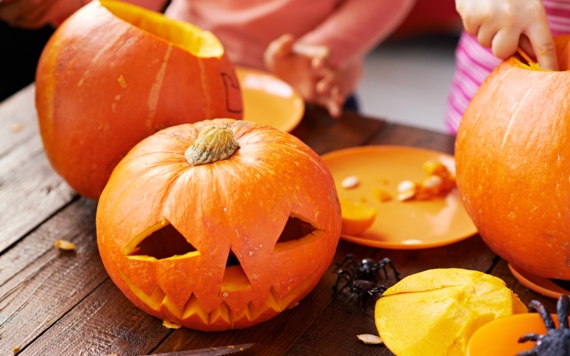 Three Halloween pumpkins on a table with two plates besides them 