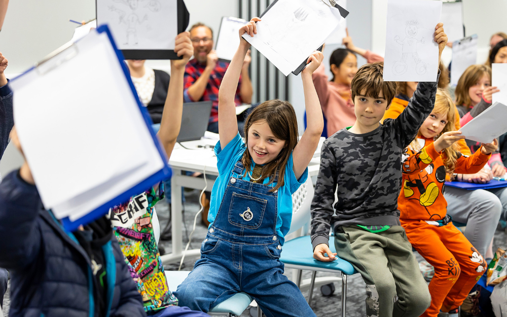 children lift drawings into the air during a session at the Wokingham Children's Book Festival