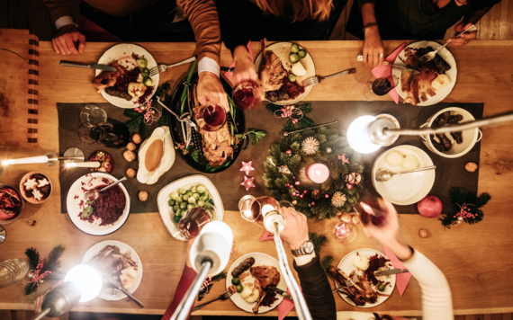 A top view of a table with Christmas food and hands raising a glass 