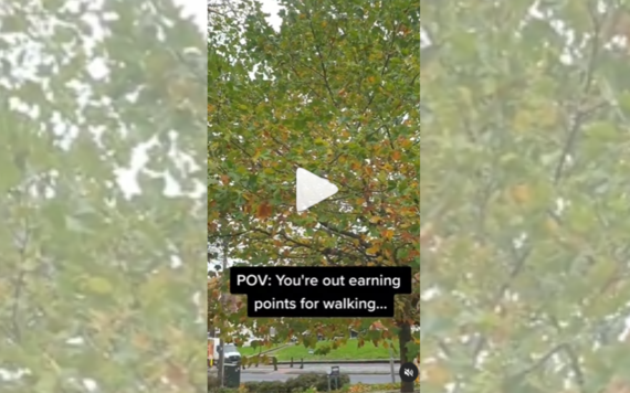 Still from a video with play button on top - trees in foreground and path in background with text overlay POV you're earning points for walking