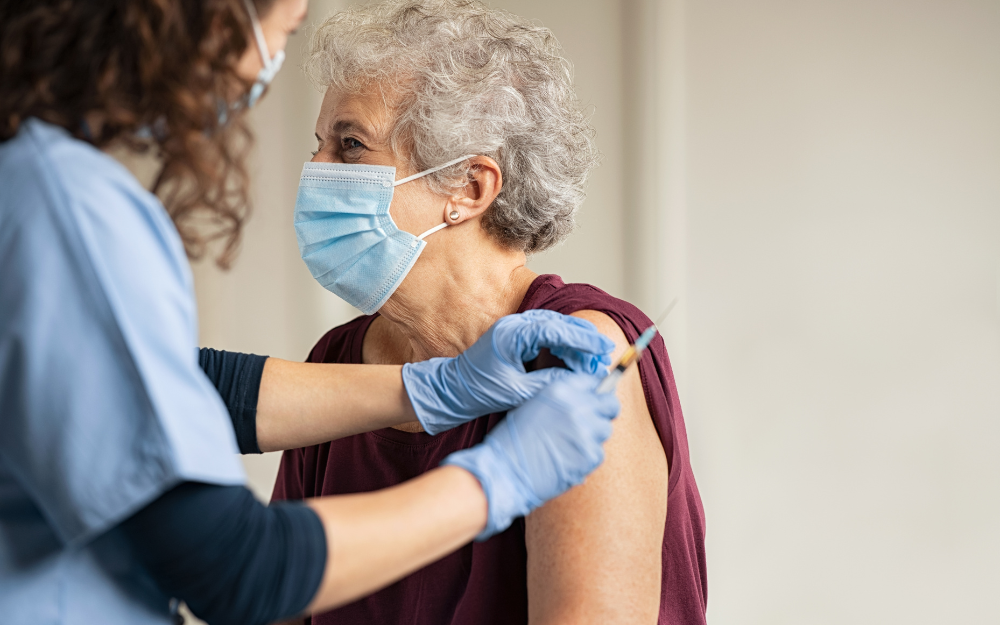 An older woman in a facemask gets vaccinated by a nurse