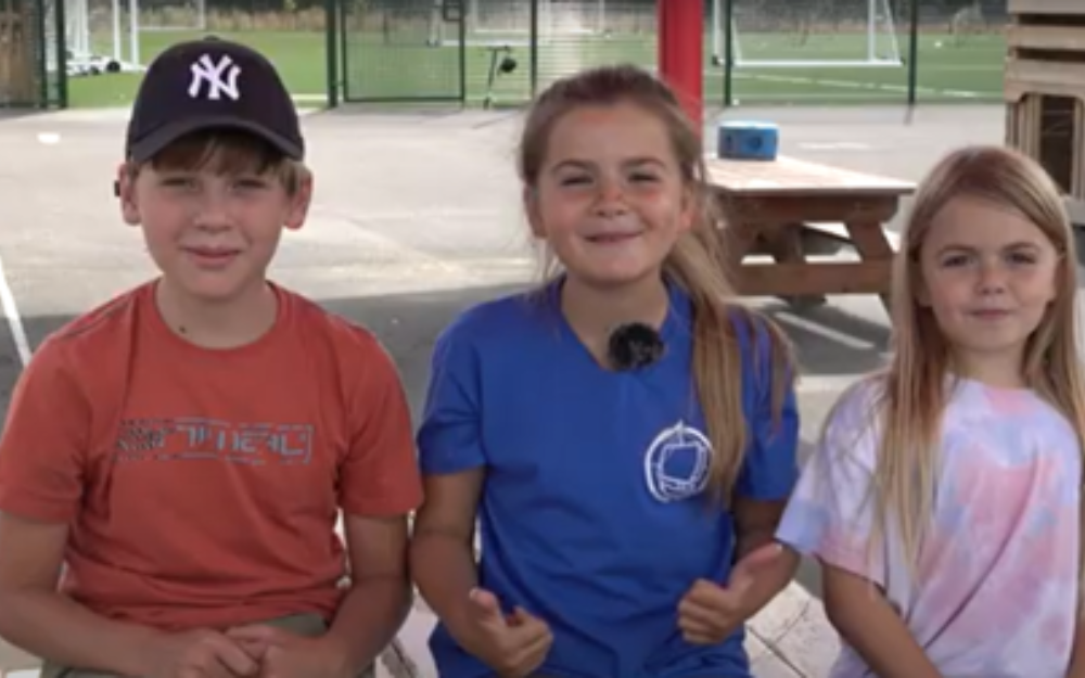 Three children sat on a playground at a holiday, activity and food programme event