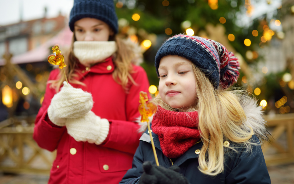 Two girls wrapped up warm in front of an outdoor Christmas tree, holding festive items